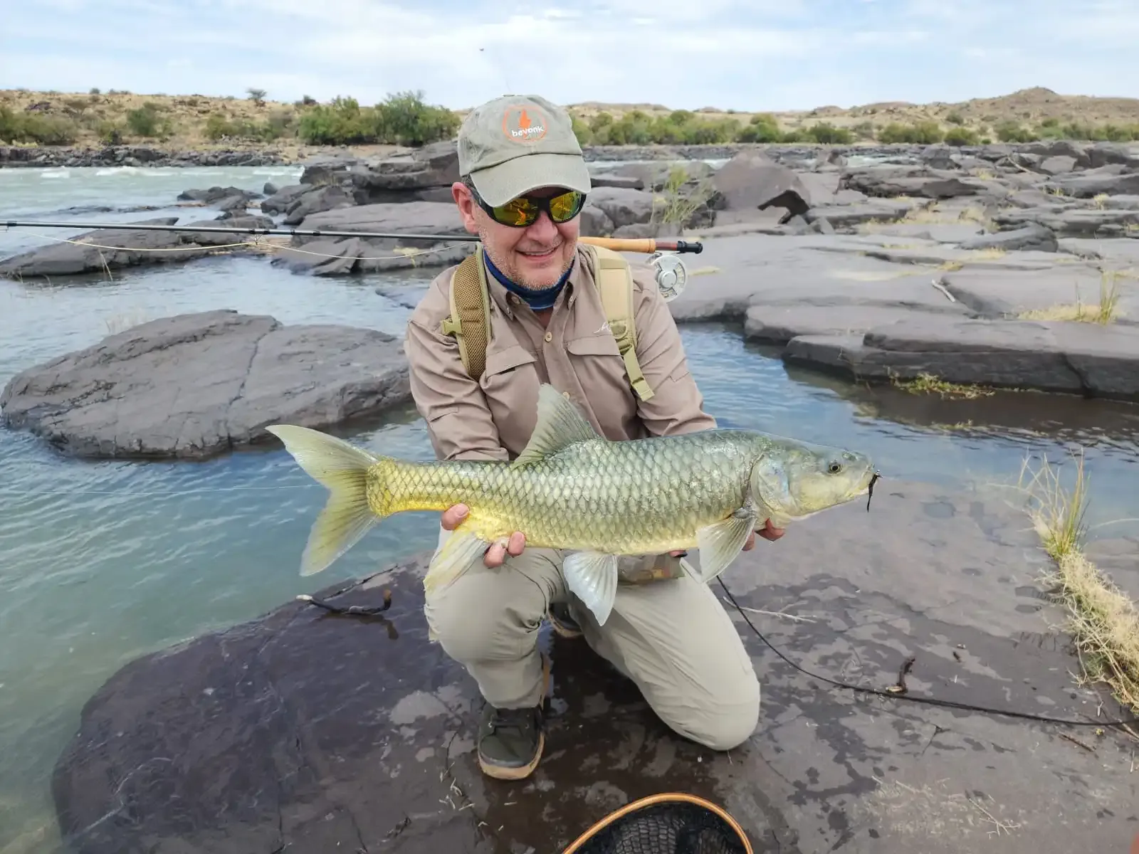 An angler holding a yellowfish on the rocky riverbank