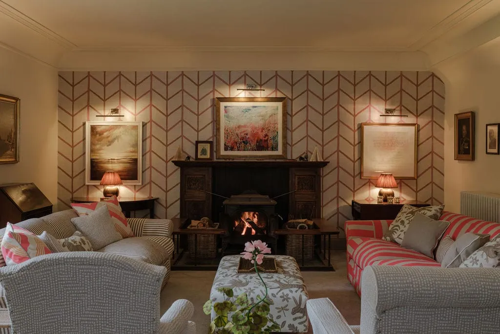 A sitting room with herringbone wallpaper, a fireplace and paired sofas