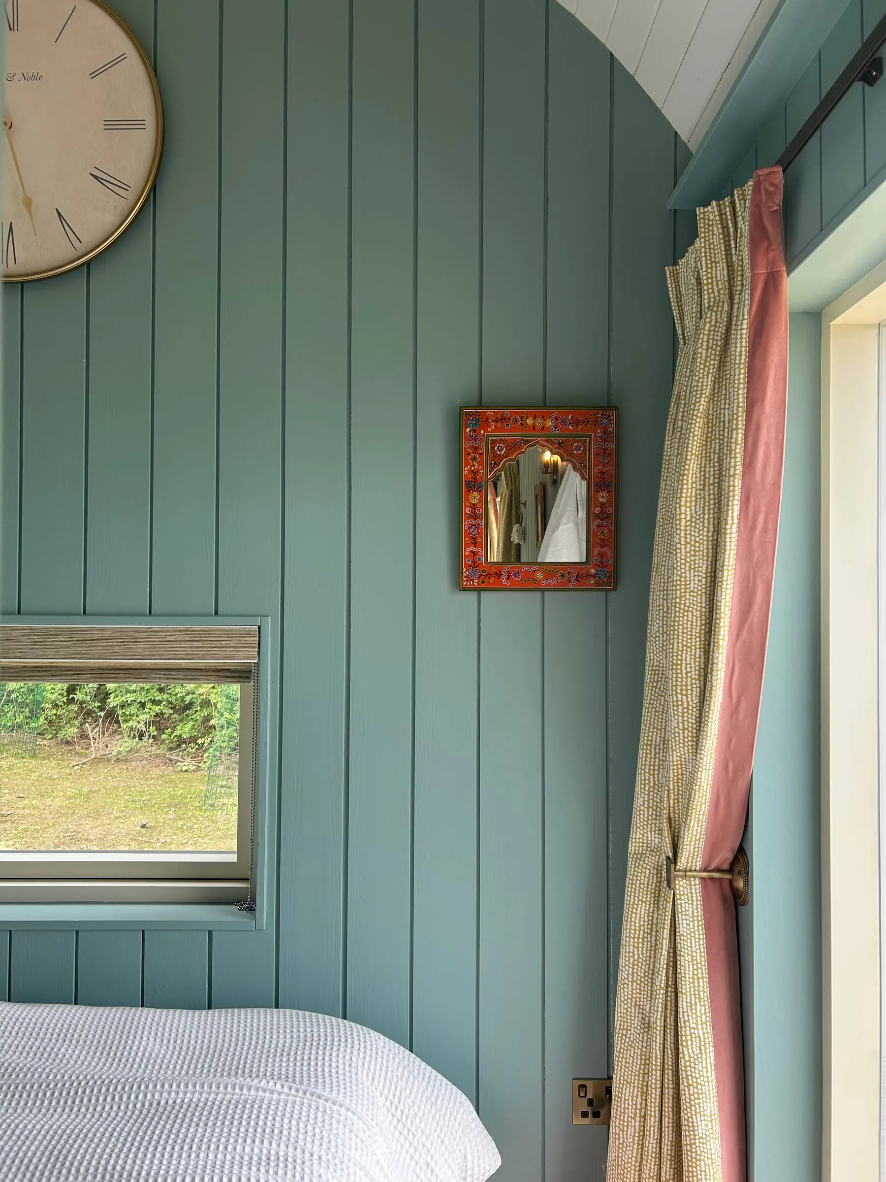 A pale blue bedroom wall with a patterned curtain at Milkwood