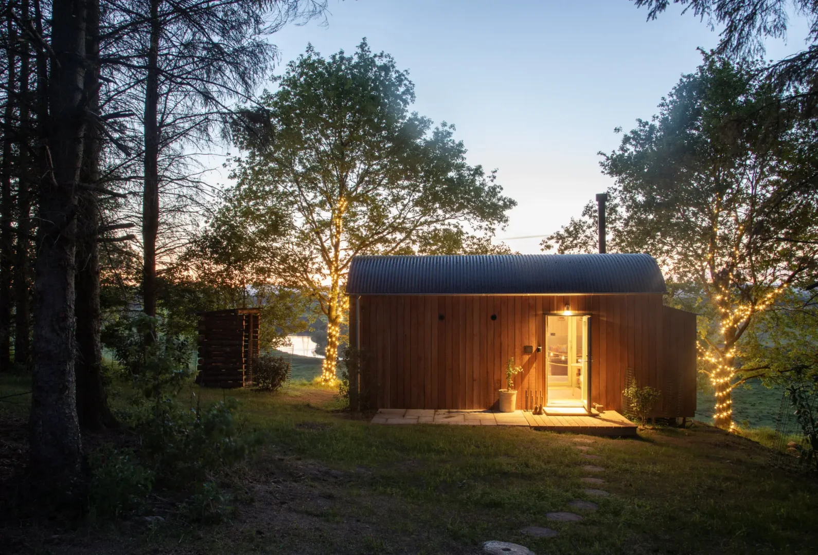 Milkwood cabin glowing at dusk beneath fairy-lit trees