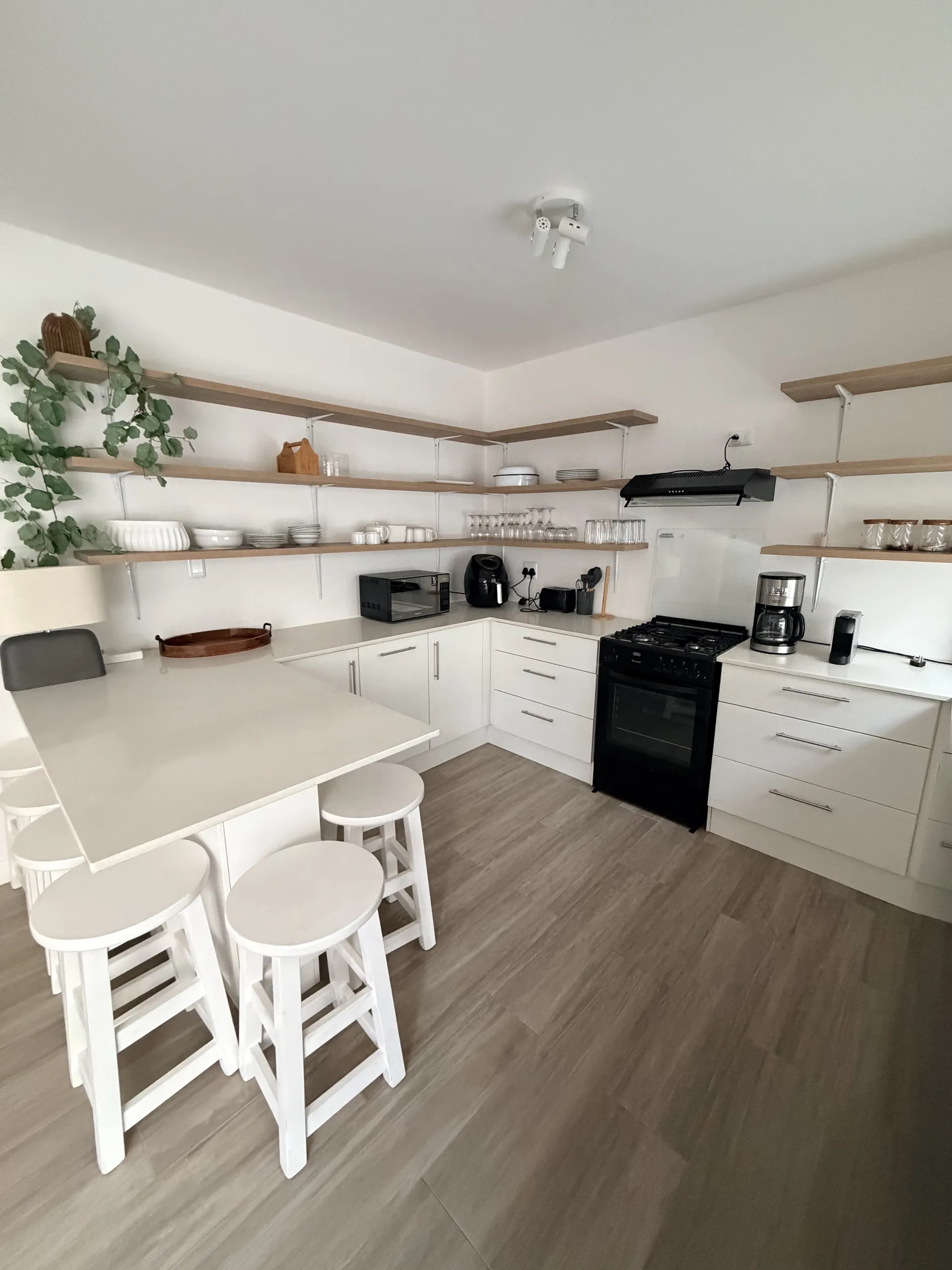 Fully equipped kitchen with open wood shelves and breakfast stools