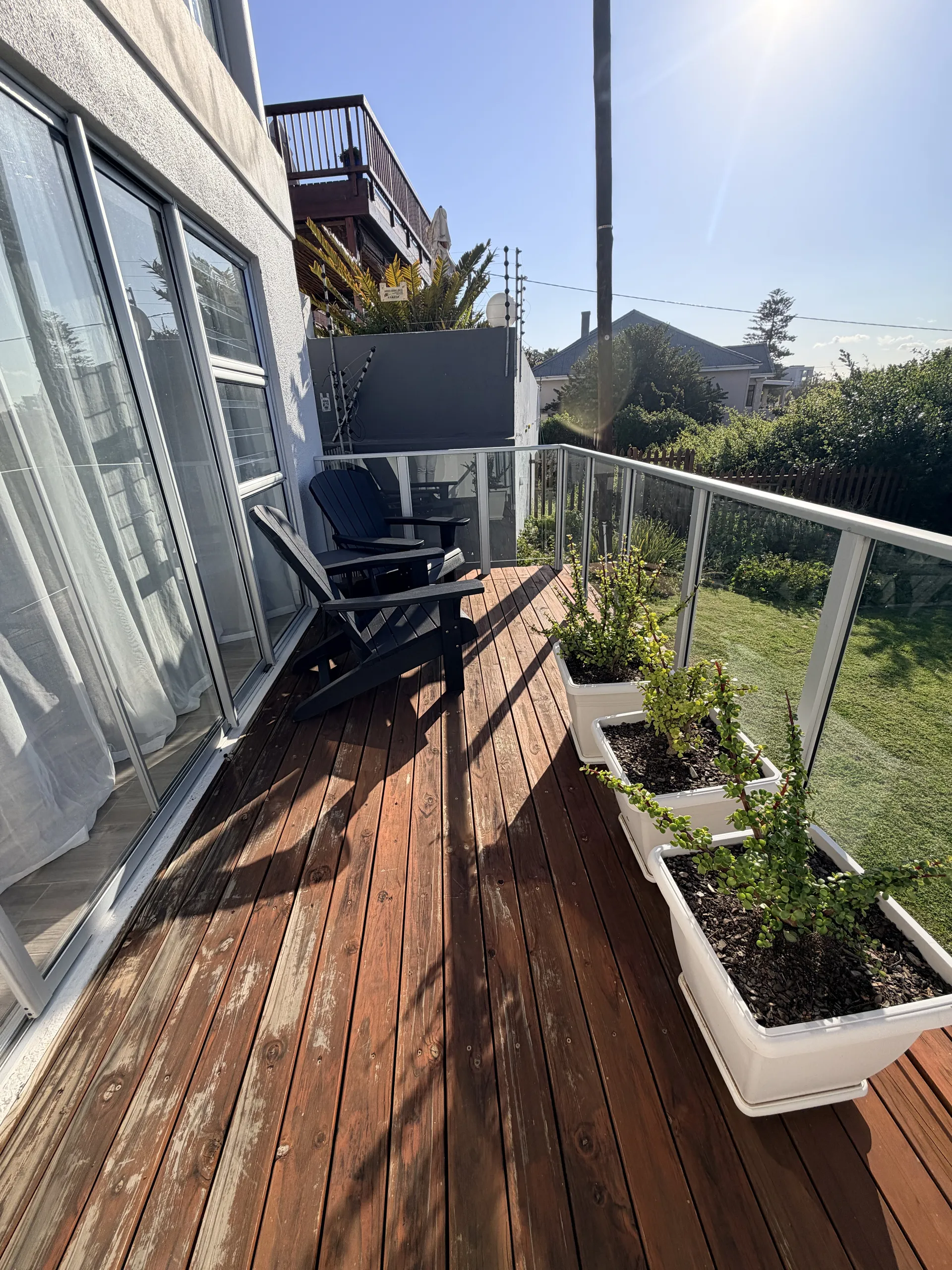 Wooden balcony with a glass railing and Adirondack chairs